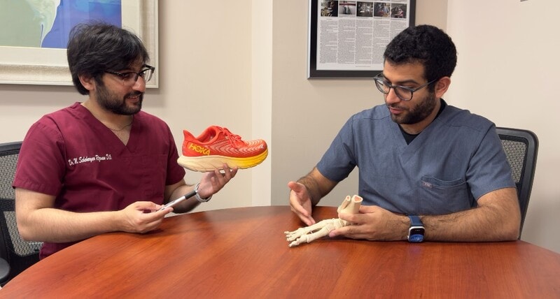 One physician holding a sneaker and oen physician holding a model of bones of a foot